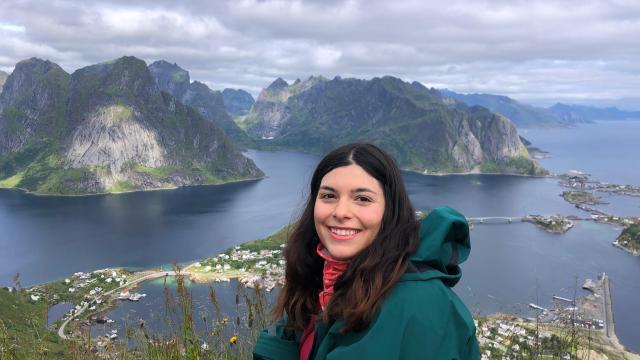 a woman in a raincoat sat on a rock with a view of an archipelago